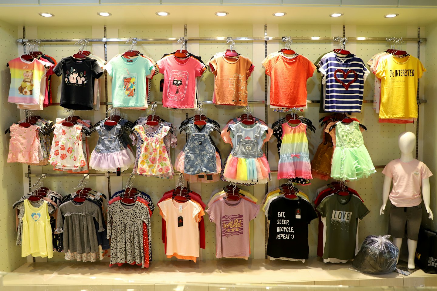 Des vêtements pour enfants sont suspendus sur des portants à côté d'un mannequin de magasin.