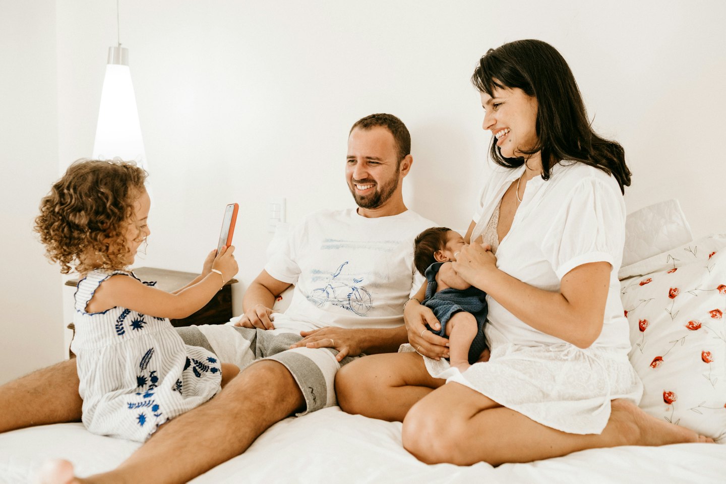 Femme souriante allaitant un bébé, un homme se tient à proximité et un enfant tient un téléphone.