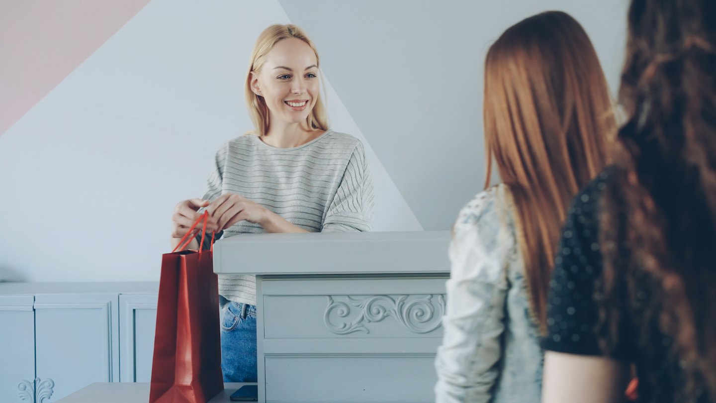 Un vendeur souriant tient un sac de courses au comptoir.