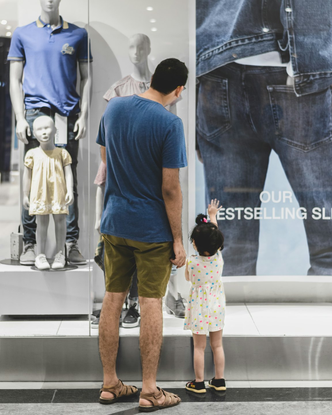 Un homme et un enfant regardent un jean dans la vitrine d'un magasin.